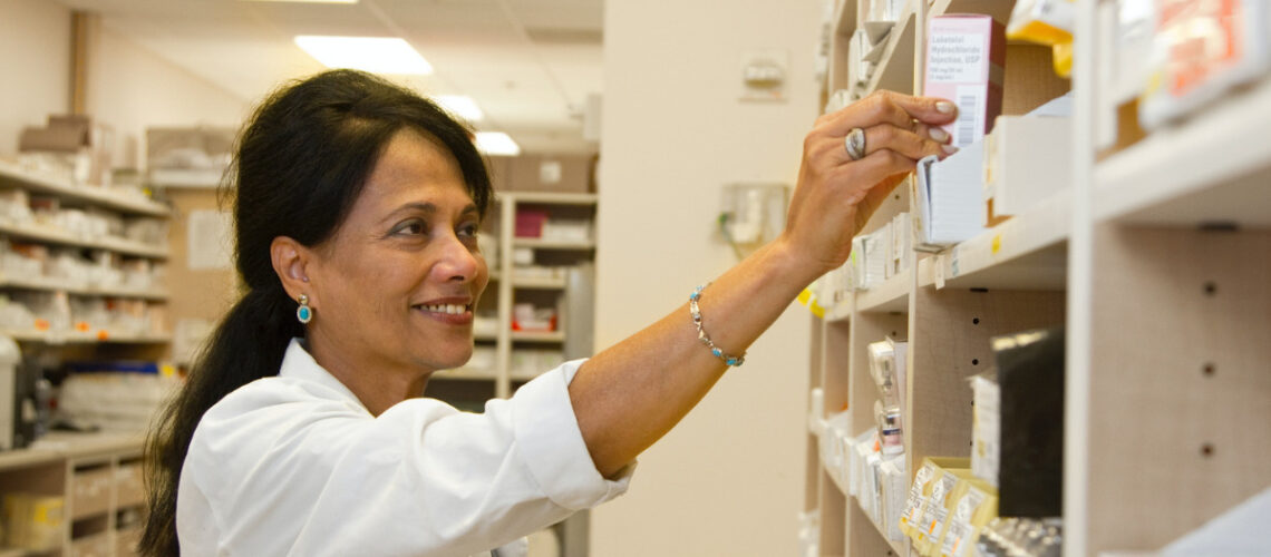Pharmacist smiling reaching for pills on a shelf