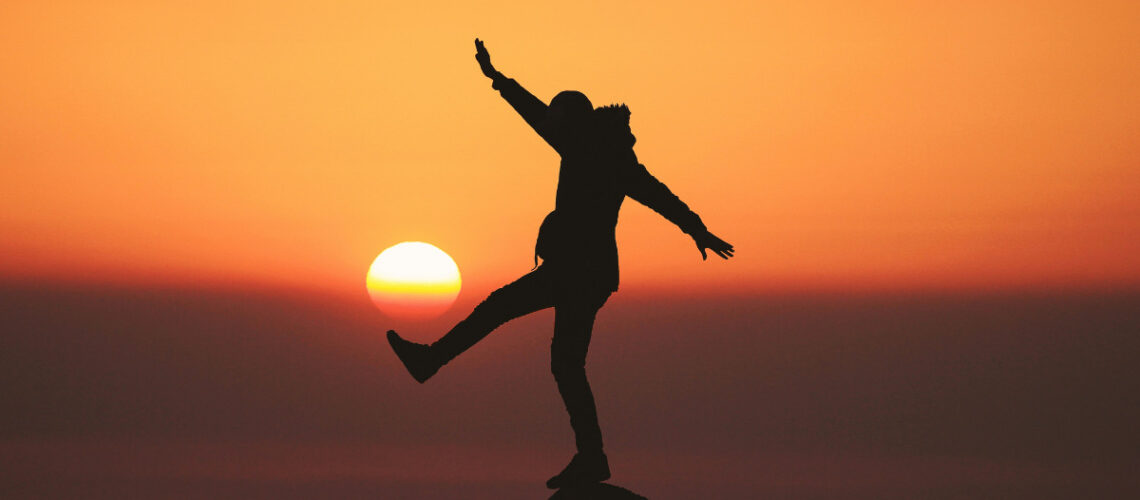man balancing on a rock with a sun setting behind him